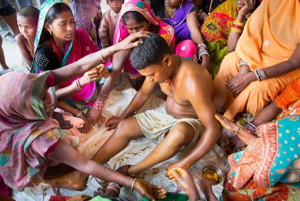 A Nepalese groom, stripped to the waist, is surrounded by women as he is prepared for his wedding.
